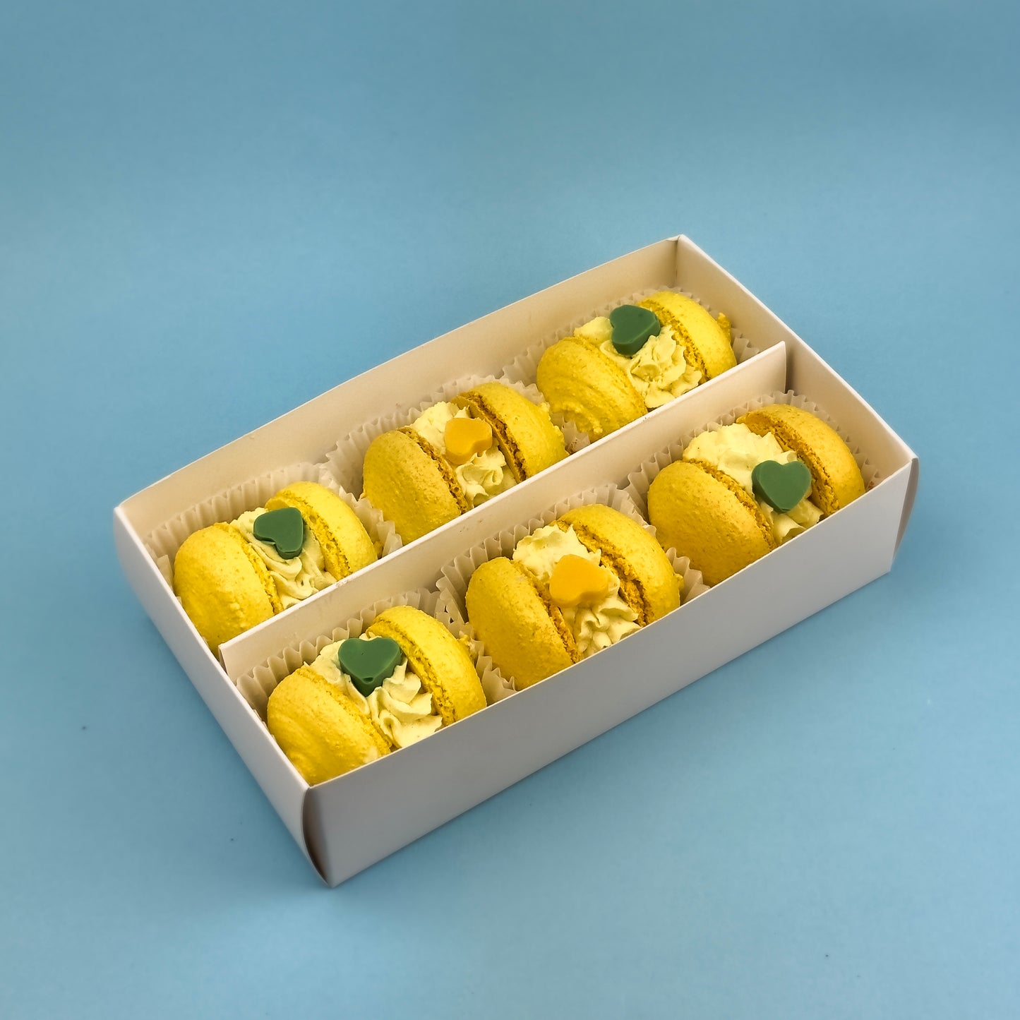 Top view of Banana-Caramel Macarons box showcasing 6 perfectly decorated macarons inside an elegant gold box.

