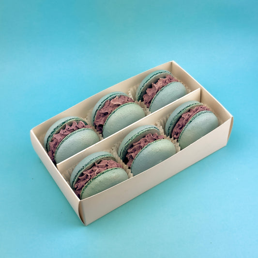 Box of 6 Blueberry Lemon Macarons in a golden-lid packaging, featuring delicate almond shells filled with blueberry puree and lemon curd, displayed on a pastel purple background.